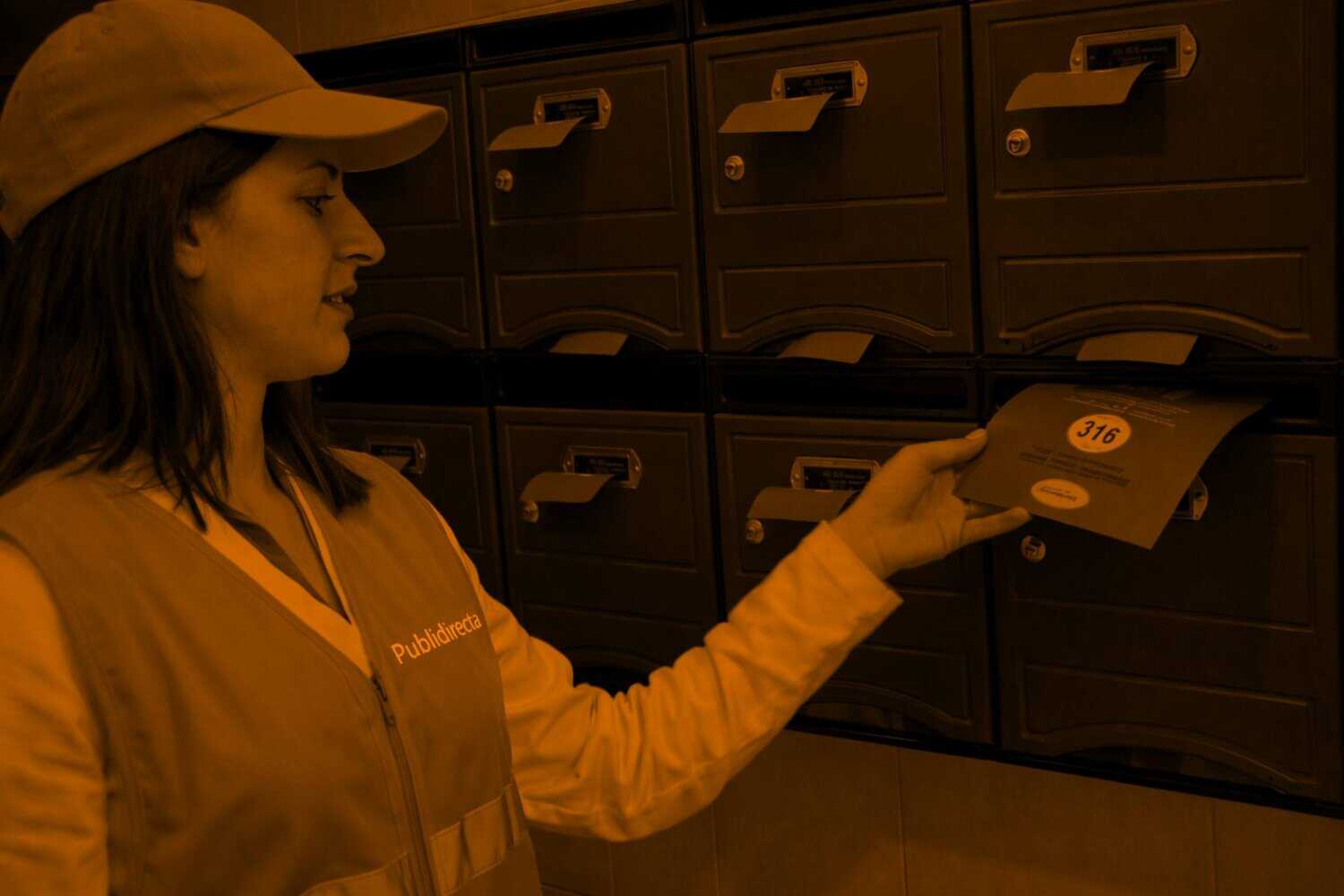 Repartidora de Publidirecta realizando buzoneo en Barcelona con folletos en buzones exteriores de un edificio.