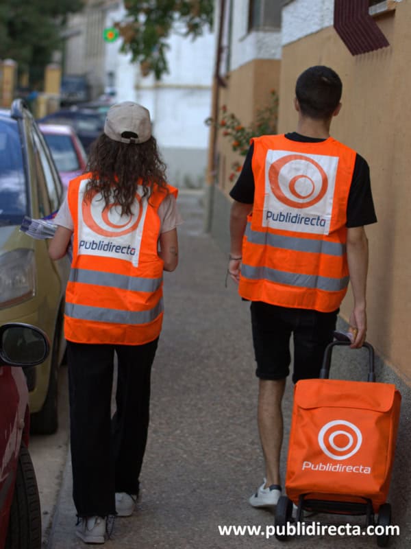 Dos repartidores de Publidirecta caminando por una calle residencial para realizar buzoneo en Madrid.