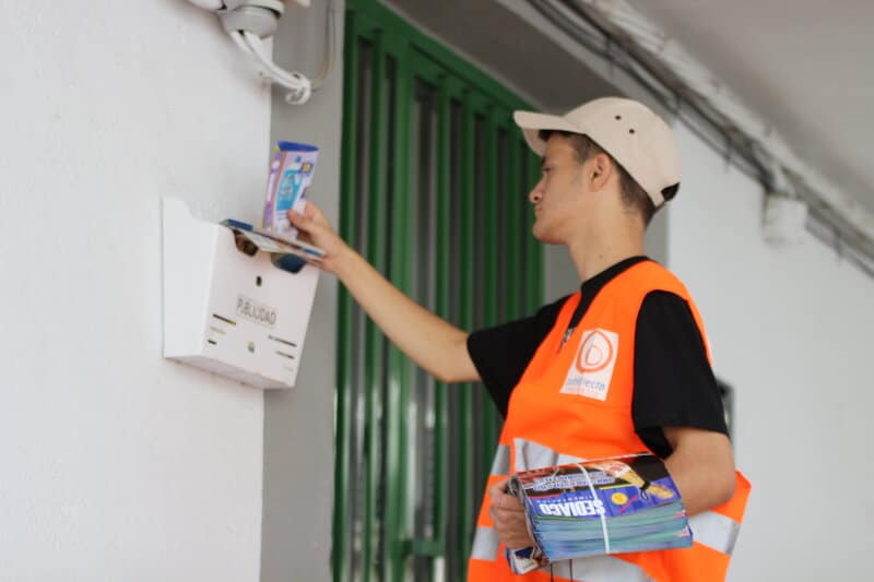 Repartidor de Publidirecta colocando folletos en buzones de una vivienda unifamiliar durante un servicio de buzoneo en Madrid.